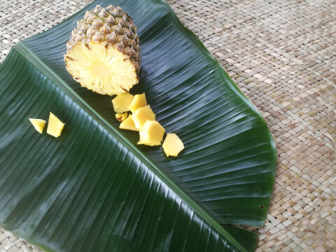 Pineapple and its slices placed in a green banana leaf.