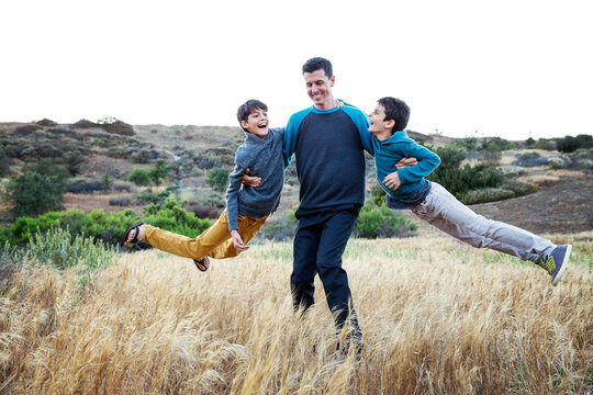 Father Twirling His Two Sons Outside in Open Field