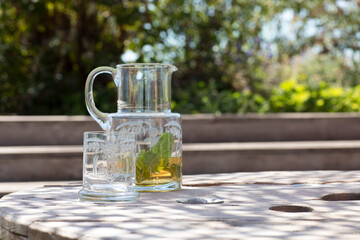 A vintage etched glass carafe pouring healthy homemade juice with mint leaves into a glass outside in a natural environment on a sunny day in summer
