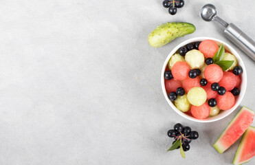 Salad of fresh watermelon balls, cucumber with black currant in a bowl on a light background top view copy space