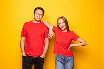 Portrait of cool couple in red shirts looking at camera isolated on yellow background.