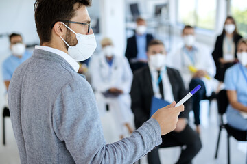 Businessman wearing face mask while giving a presentation at conference hall.