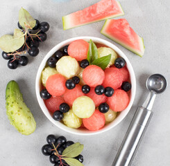 Salad of fresh watermelon balls, cucumber with black currant in a bowl on a light background top view
