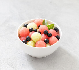 Salad of fresh watermelon balls, cucumber with black currant in a bowl on a light background