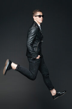 Trendy stylish handsome man in sunglasses jumping in studio