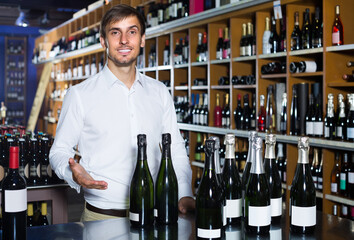 portrait of young glad male customer taking bottle of wine in store