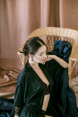 Young girl with dark hair in dark underwear and a silk peignoir on a wicker chair