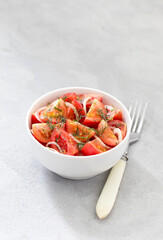 Vegetable salad of fresh tomatoes with onions and dill in a bowl on a light background