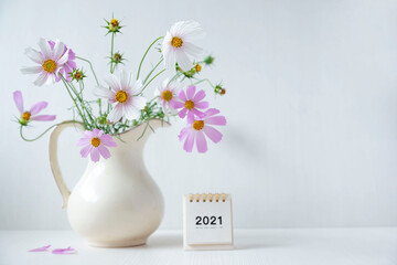 A bouquet of fresh flowers in a light jug in a home interior and a calendar for 2021.