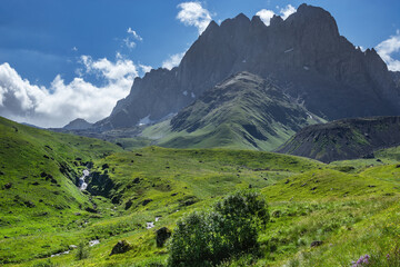 Obraz premium Rocky mountain top, river with waterfall and grassy valley. Chaukhi, Georgia