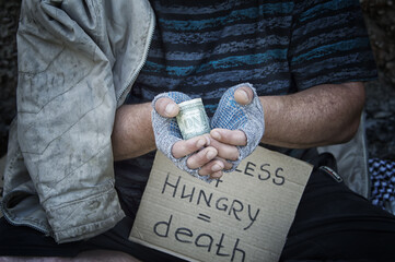 A dollar in the hands of a homeless man in gloves. Poverty, hunger, unemployment.