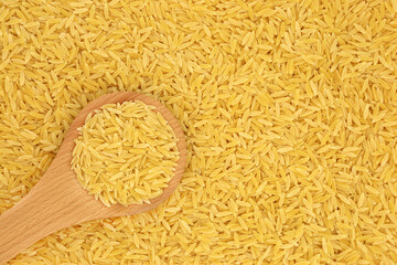 Italian orzo pasta in a wooden spoon & forming a background. Suitable for vegan & vegetarian diet, gluten free & high in fibre, vitamins and minerals. Flat lay, top view.