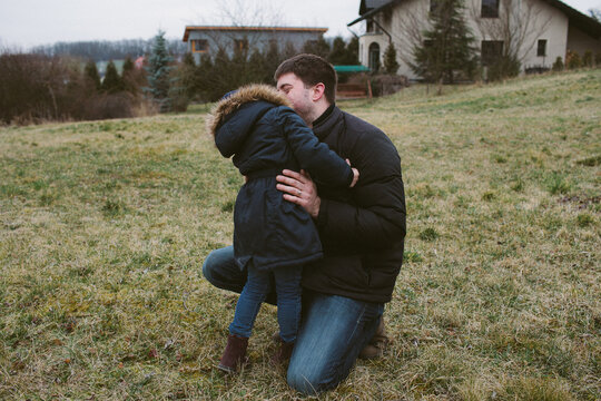 Father kneels down to hug and kiss his little daughter while on a walk in the countryside.