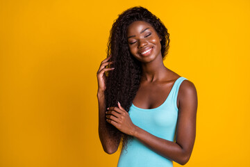 Photo portrait of young african american woman brushing hair with hands with closed eyes isolated on vivid yellow colored background