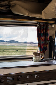A coffee cup sits on the dash of a camper can with Idaho's Rocky Mountains in the background