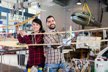 Cheerful positive team of aircraft enthusiasts holding sports airplane models in workshop