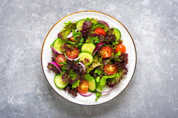 Healthy vegetable salad of cherry tomatoes, cucumber slices, green and purple lettuce leaves, onions and olive oil in plate on concrete table Top view Flat lay Diet, mediterranean menu Vegan food