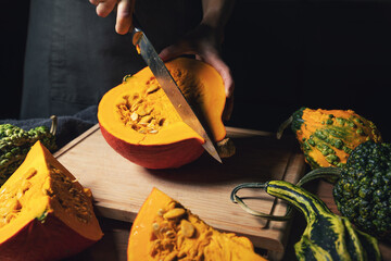 fall season harvest - woman cutting pumpkin with knife for cooking on wooden board