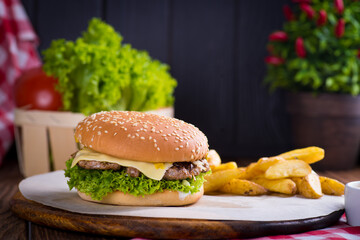juicy burger on a plate with a red napkin and potatoes on a black wooden background