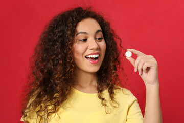 Emotional African-American woman with vitamin pill on red background