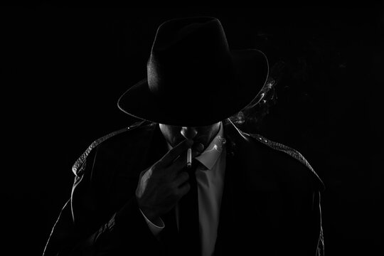 Old fashioned detective smoking cigarette on dark background, black and white effect