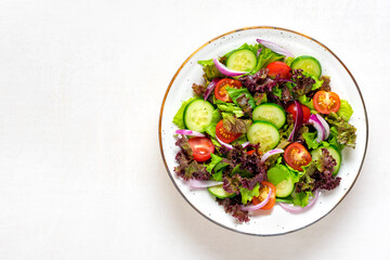 Healthy vegetable salad of red cherry tomatoes, cucumber slices, green and purple lettuce leaves, onions and olive oil in plate on white table Top view Flat lay Diet, mediterranean menu Vegan food