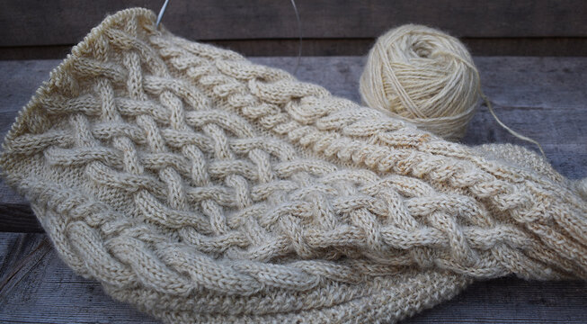 Zopfmuster wird gestrickt, Strickst&uuml;ck mit selbst gesponnenem Wollgarn aus Schafwolle in wollwei&szlig; auf grauem Hintergrund, stricken als hobby und f&uuml;r Strickwaren Anbieter, winterlich