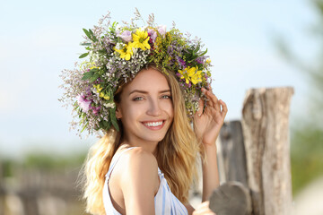 Young woman wearing wreath made of beautiful flowers outdoors on sunny day