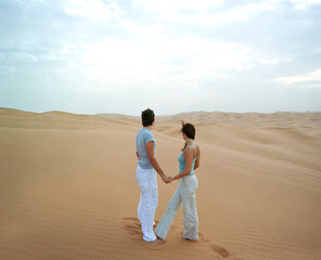 Couple standing together in sand dunes.