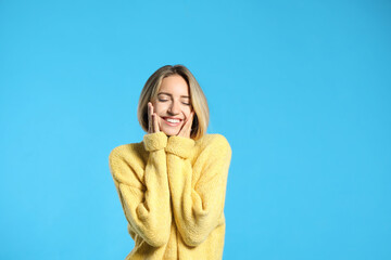 Beautiful young woman wearing knitted sweater on light blue background