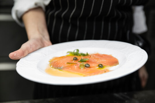 Chef_&Ocirc;&oslash;&Omega;&Ocirc;&oslash;&Omega;s hand holding a plate with salmon carpaccio