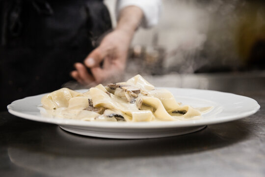 Plate of pappardelle pasta on counter with chef behind