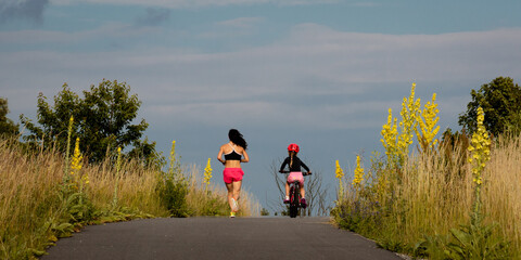 mother running and daughter cycling seen from behind on a countryside road