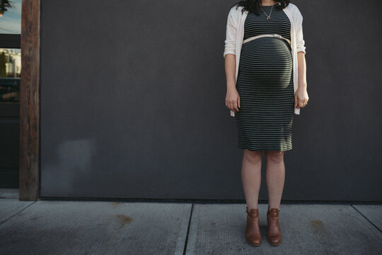 Pregnant woman standing near grey wall outside - belly bump