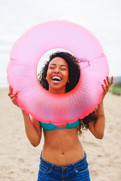 Happy african american woman holding a pink inner tube on the beach.