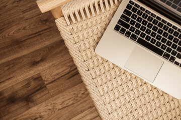 Laptop keyboard and wicker bench on wooden floor. Flat lay, top view home office workspace