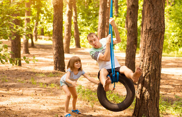 Happy child daughter pushing father on tire swing in garden