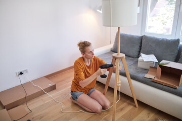 Woman assembling furniture in new apartment, moving in and being hardworking.