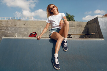 Summer. Skater Girl Sitting On Concrete Skate Ramp At Skatepark. Female Teenager In Casual Outfit With Skateboard. Urban Sport As Lifestyle For Active Teens In City. - obrazy, fototapety, plakaty