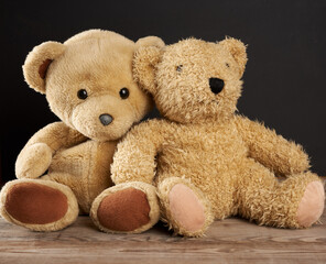 two brown teddy bears are sitting on a brown wooden table, black background