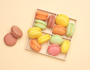wooden box and baked multi-colored macarons cookies on a beige background