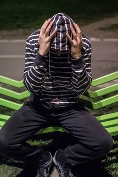 problematic, the hooded man on a bench holding his head