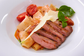 Close up view on cooked pasta and sliced duck breast with sauce and parmesan with copy space. Shallow dof.