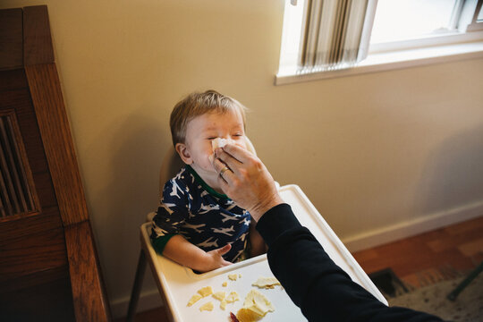 Toddler boy getting his nose wipes sitting in highchair