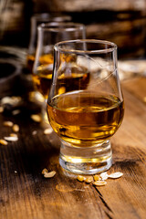 Small tasting glasses with aged Scotch whisky on old dark wooden vintage table with barley grains