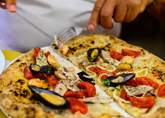 Eating of Italian pizza with sea food, small red tomatoes and fresh basil