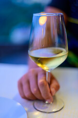 Hand with glass of cold dry white wine served outdoor in cafe at night in Italy