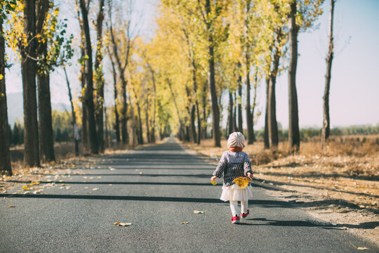 A baby girl walking on a road in autunm