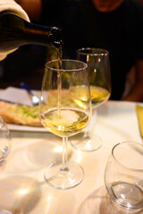Pouring in glass  cold dry white wine in outdoor cafe at night in Italy