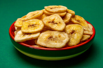 Healthy snack, crispy dehydrated unsugared banana chips in bowl on green background